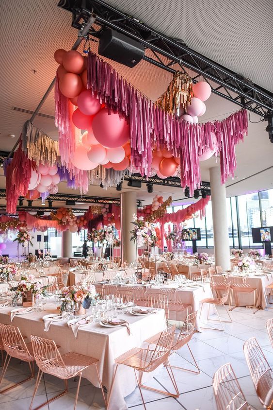 a bright modern wedidng reception space with blush tables and blooms, pink and blush balloons and colorful tinsel fringe