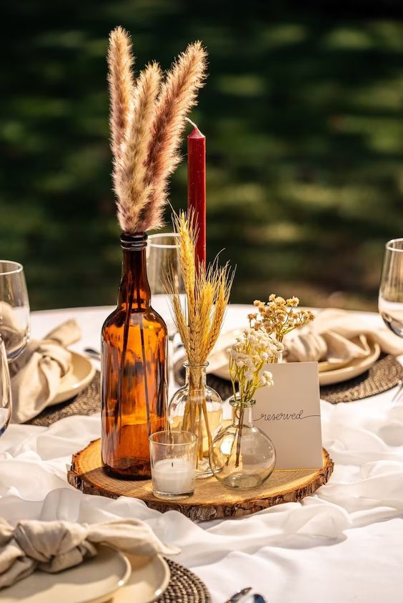 a western wedding centerpiece of a wood slice, a candle, bottles with dried grasses and a card is a lovely and easy to DIY arrangement