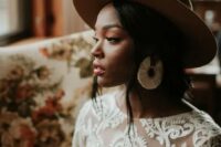 a boho bridal look with a boho lace wedding dress with a high neckline, statement yarn earrings and a brown hat is amazing
