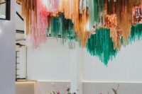 29 a chic modern wedding reception space with pink, rust, orange and green streamers over it and bold pink blooms on the table
