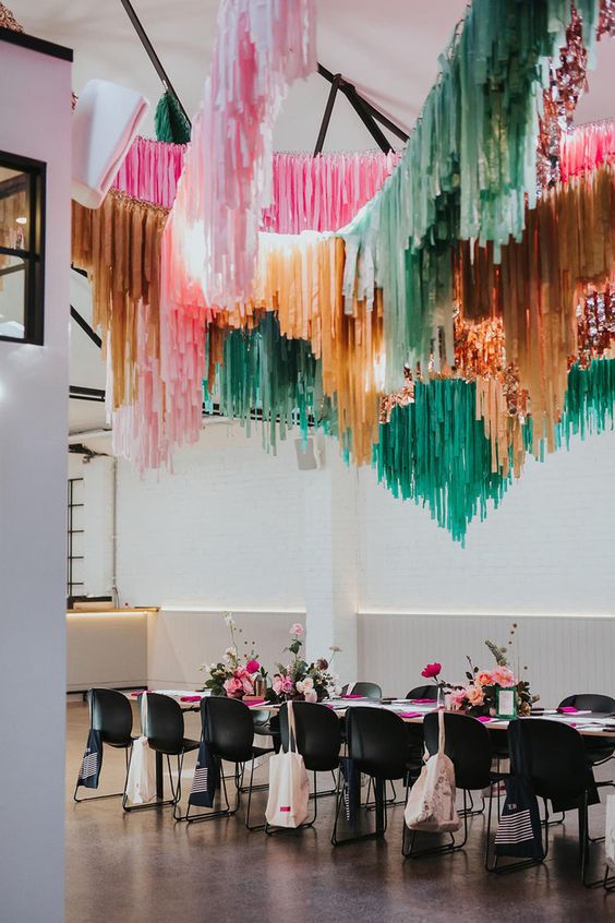 a chic modern wedding reception space with pink, rust, orange and green streamers over it and bold pink blooms on the table