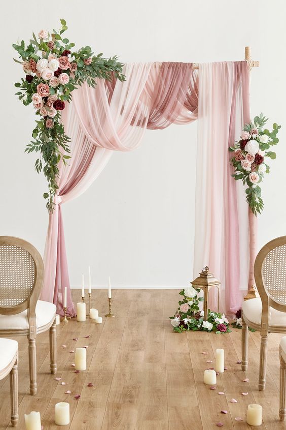 a refined wedding arch with pink, white and mauve drapes, greenery, white, pink and burgundy blooms, pillar and usual tall and thin candles