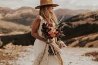 30 a boho western bridal look with an A-line wedding dress with a tulle skirt, a deep neckline and no sleeves, a beige hat and a cool colored bouquet