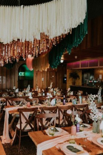 a chic wedding reception space with blush table runners and neutral blooms, white, gold and emerald streamers over it is fantastic