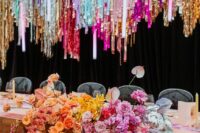 31 a fantastic and bright wedding reception space with colorful tinsel streamers and matching colorful blooms on the table