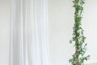 31 a simple and classy wedding backdrop with white drapes and greenery and white blooms, pillar candles on the floor is a lovely idea