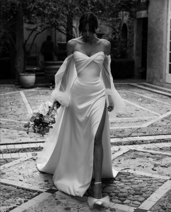 an off the shoulder wedding dress with a draped bodice and long tulle sleeves plus a skirt with a thigh high slit and a train
