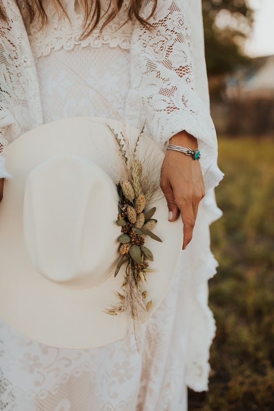 a creamy bridal hat with dried grasses and greenery plus a silver bracelet with an emerald for a western or boho bridal look