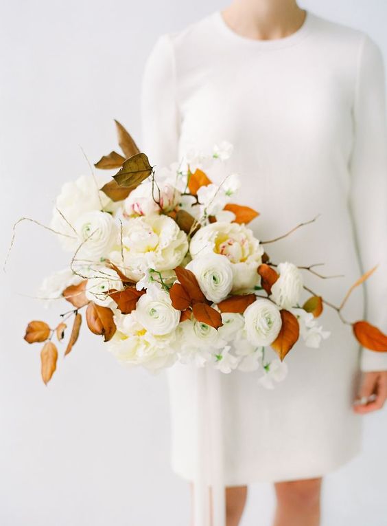 a modern fall wedding bouquet with white peony roses, ranunculus and bright fall leaves is a gorgeous solution for a fall bride