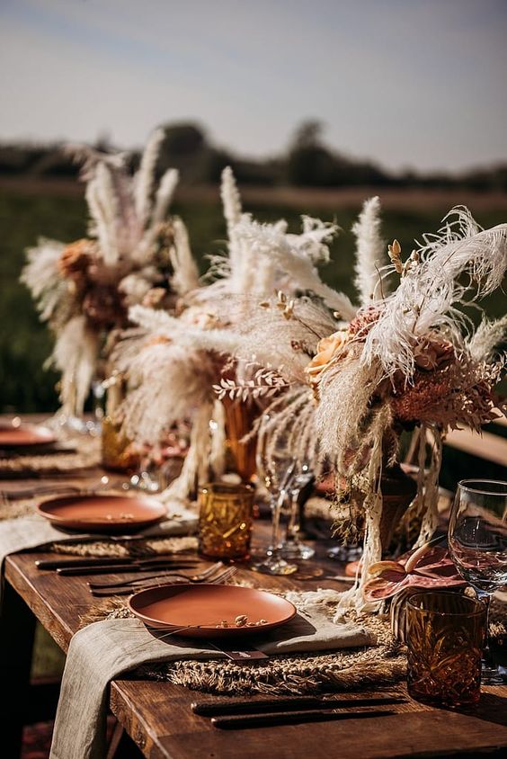 a western wedding table setting with dried grasses and fresh peachy blooms, terracotta plates, woven placemats, amber glasses