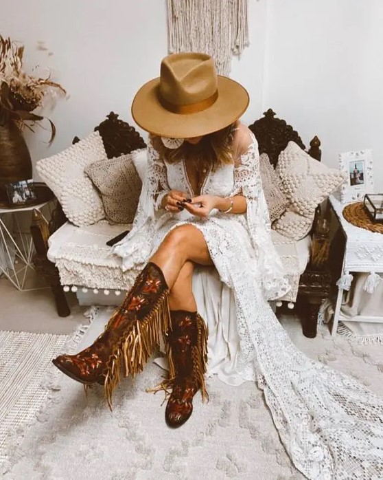a fantastic western bridal look with tall floral pattern and gold fringe cowboy boots, a boho lace A-line wedding dress with bell sleeves and a tan hat