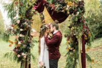 33 a sophisticated fall wedding arch with burgundy velvet drapes, bold blooms, fir branches and bold fall leaves for a boho wedding
