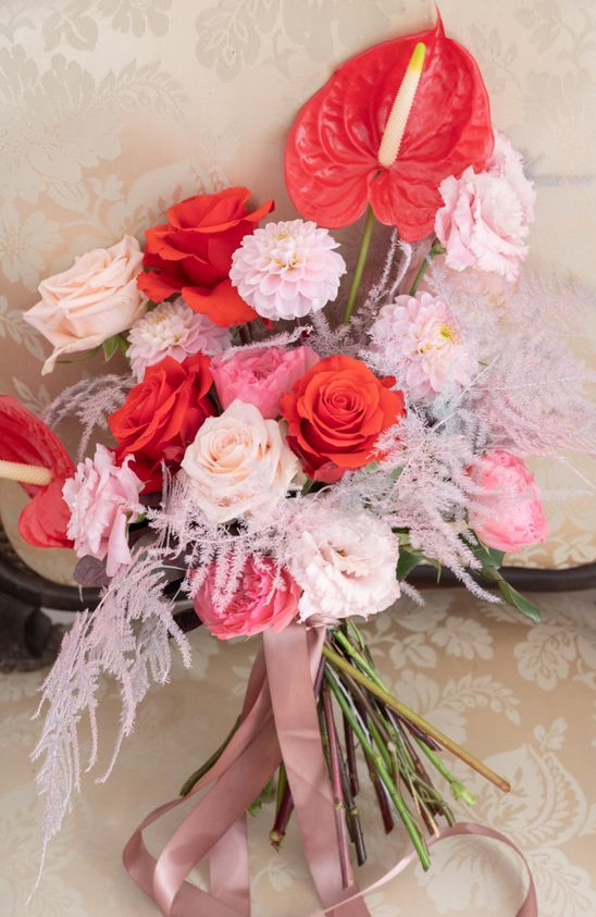 a bright modern wedding bouquet of peachy, pale pink and red roses, peony roses, red anthurium and mauve ribbons is amazing