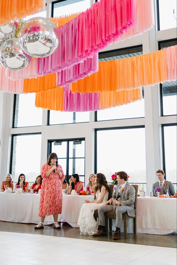 a modern wedding reception space with neutral tables but bright blooms and colorful streamers over the tables