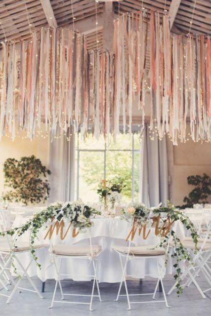a neutral wedding reception space with white reception tables, greenery and blooms and pink and neutral streamers over the space