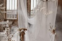 36 a super creative and fun wedding backdrop of neutral drapes, white blooms and blooming branches, pillar candles is wow