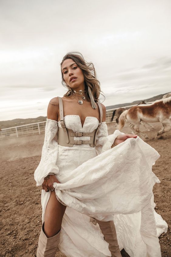 a western bridal look with a lace strapless wedding dress with puff sleeves, a grey leather corset, grey boots and statement jewelry