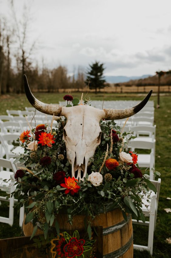 boho western wedding cermeony space with greeneyr, neutral and red blooms and a large skull on top is a lovely idea for a western wedding
