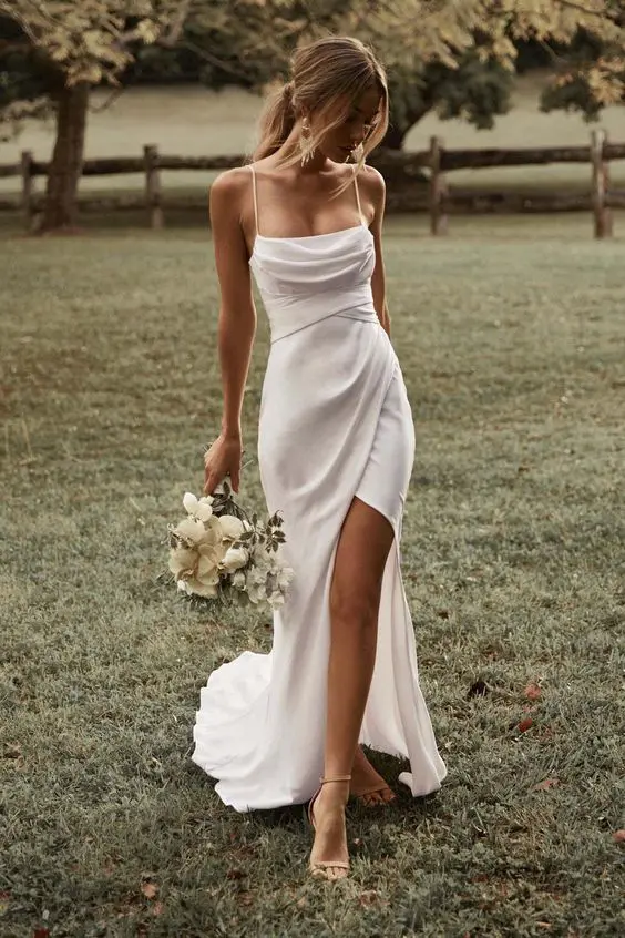 a delicate modern wedding dress with a draped bodice, spaghetti straps, a draped skirt with a slit and a train is amazing