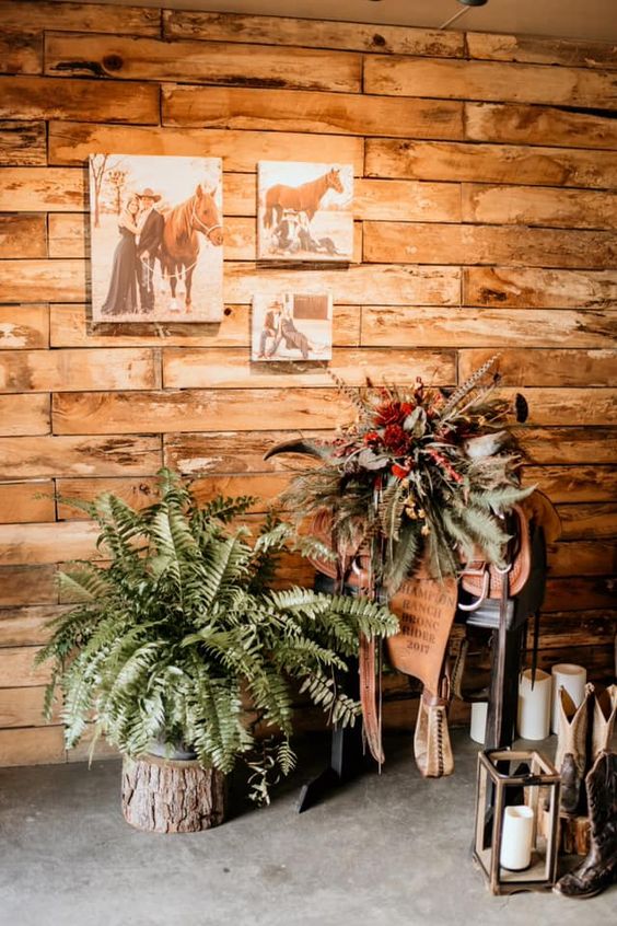 western wedding decor with ferns, bold blooms and feathers, a saddle, candle lanterns and a mini gallery wall with photos of the couple