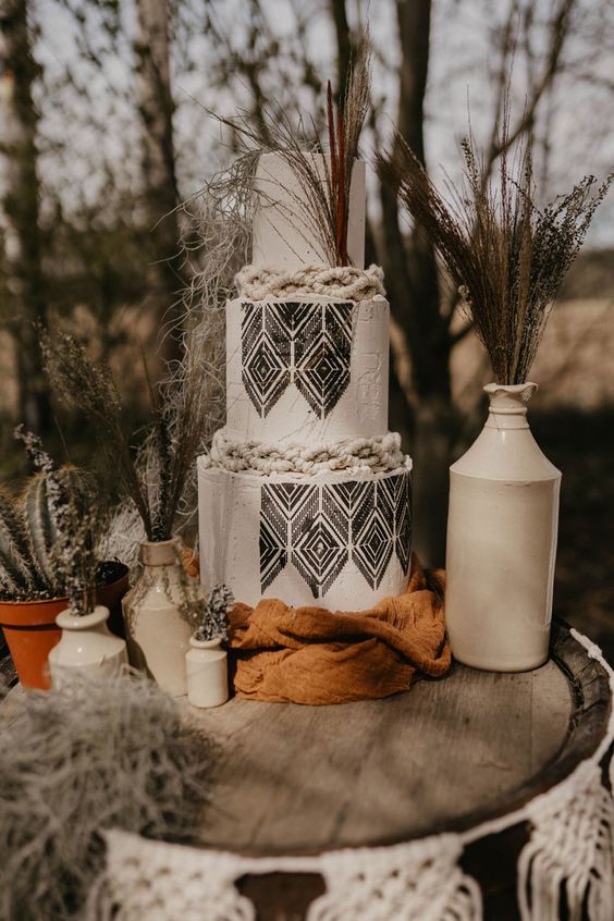 a boho western wedding cake in black and white, with texture and black pattern, with dried branches and cacti around