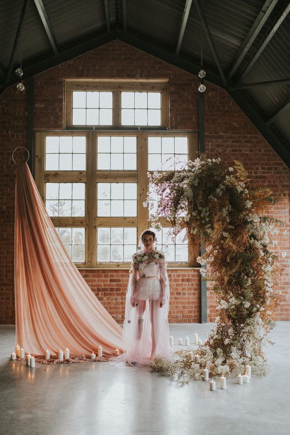 a unique wedding altar of a pink draped and a fresh and dried bloom installation, with pillar candles around is jaw-dropping