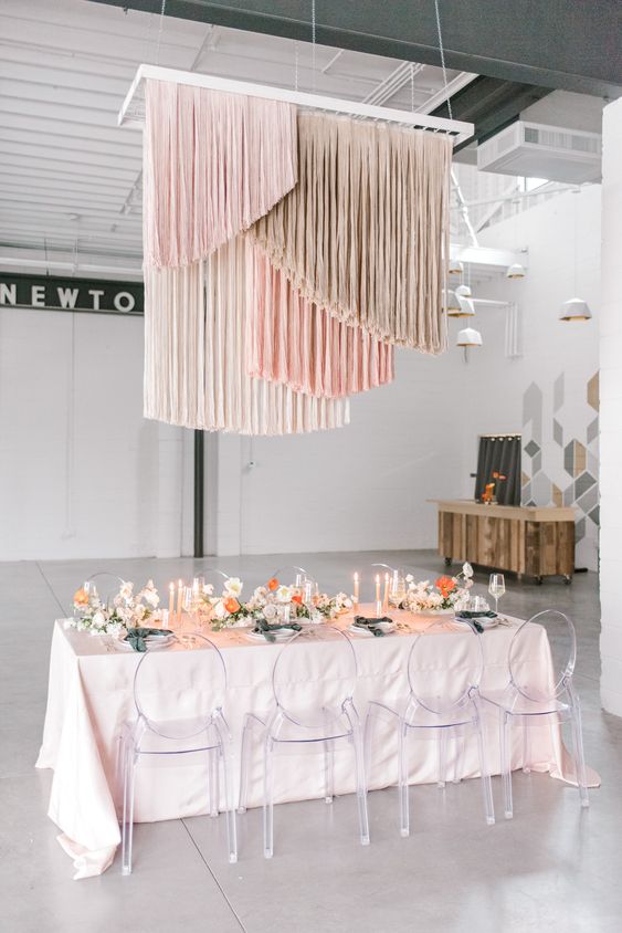 a romantic wedding reception space with a blush table and some neutral and bright blooms, blush, grey and creamy fringe over the table
