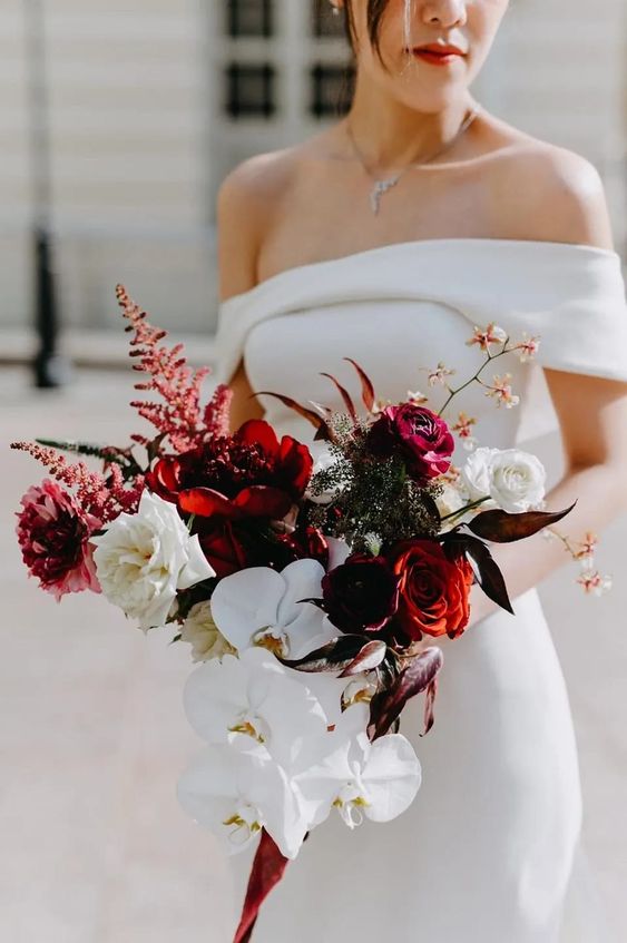 a contrasting and dramatic wedding bouquet of white orchids, red roses and peonies, white roses, amaranthus