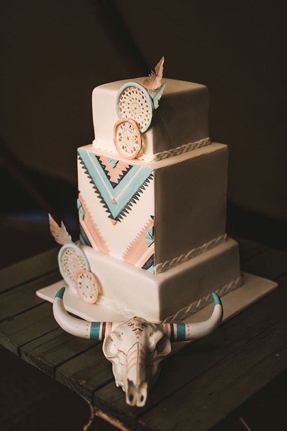 a bright boho western wedding cake with colorful geo detailing, edible embroidery hoops and feathers and a skull