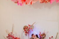41 a wedding sweetheart table with super colorful blooms and pampas grass and bright streamers over the space
