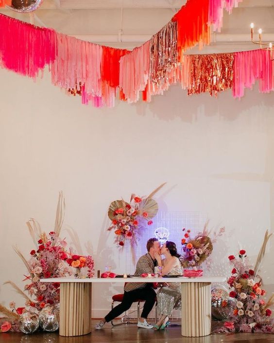 a wedding sweetheart table with super colorful blooms and pampas grass and bright streamers over the space