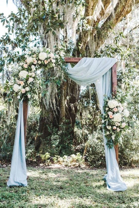 an outdoor wedding backdrop with dusty blue drapes, white blooms and greenery is a lovely idea for a spring outdoor wedding