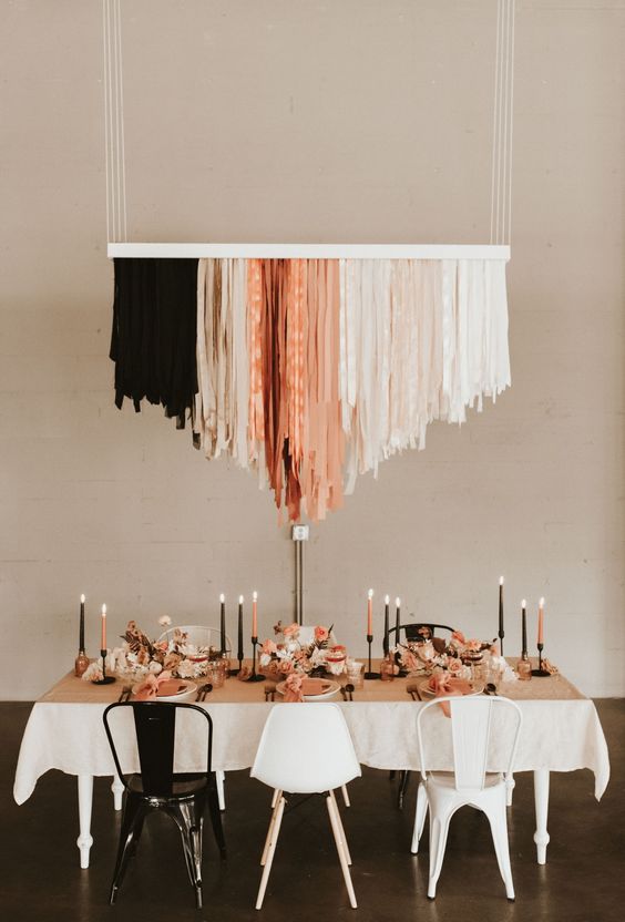 an edgy wedding reception space with a black, nuede and coral streamer chandelier, matching candles and black and white chairs