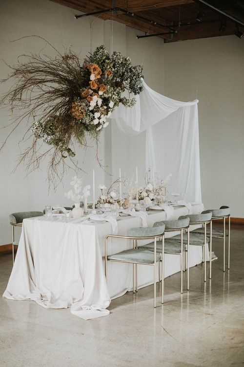 a beautiful wedding reception space with white drapes, white and coffee-colored blooms and branches, white flowers and candles
