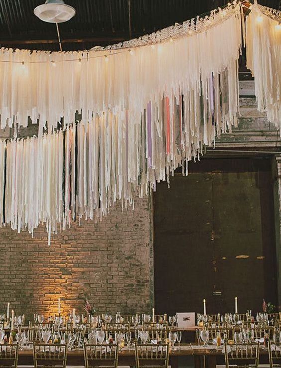 an industrial wedding reception space with brick walls, long tables and fun and cool neutral streamer decorations over the table