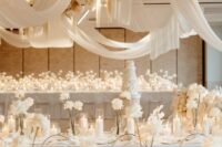 44 a creamy wedding reception space with lots of white roses and pillar candles, with creamy drapes and blooms over the space