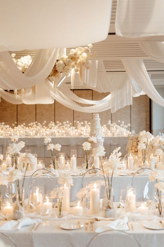 a creamy wedding reception space with lots of white roses and pillar candles, with creamy drapes and blooms over the space