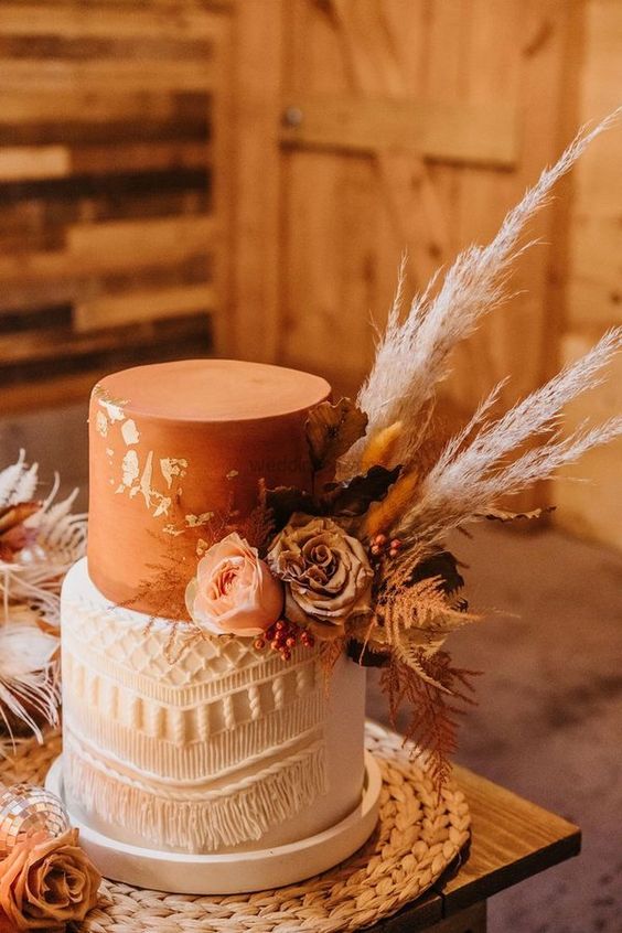 a rust and white wedding cake with gold leaf, macrame, neutral blooms, pampas grass and leaves is a cool idea for a western wedding