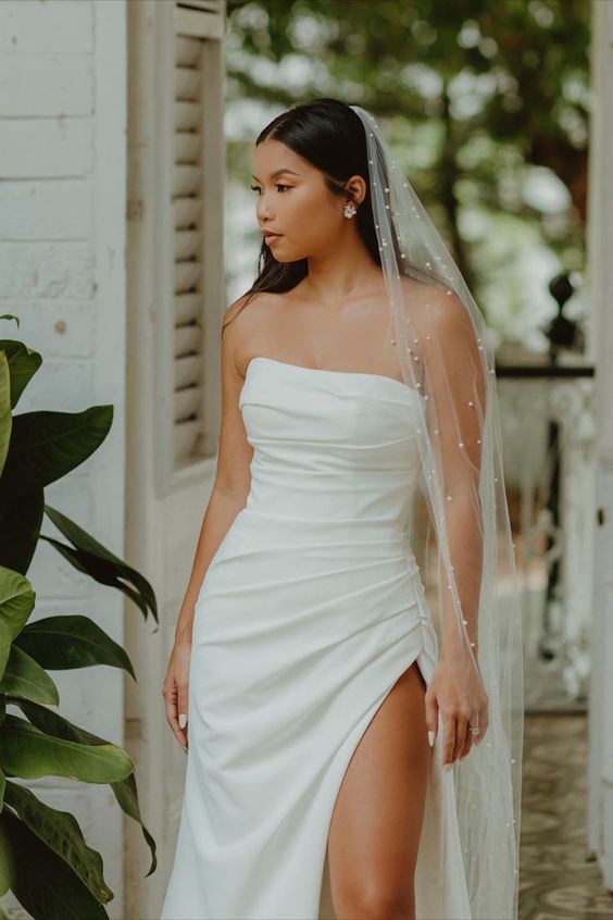 a strapless fully draped wedding dress with a thigh high slit and a pearl veila re a lovely and bold combo for a wedding