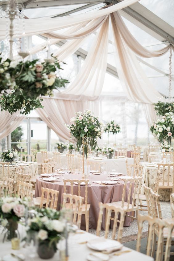 a dreamy and romantic wedding reception space with neutral drapes, mauve tablecloths, greenery and white blooms and elegant chairs