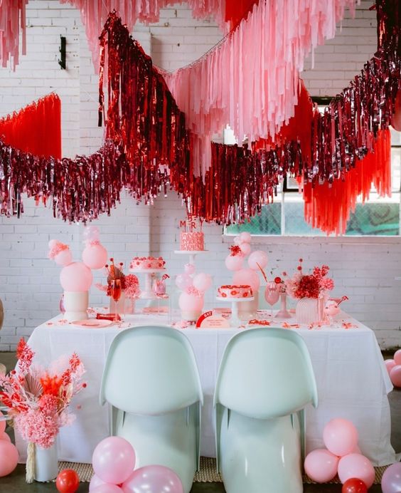 a bright pink and red wedding dessert station with pink, red and red tinsel streamers over the table is pure fun