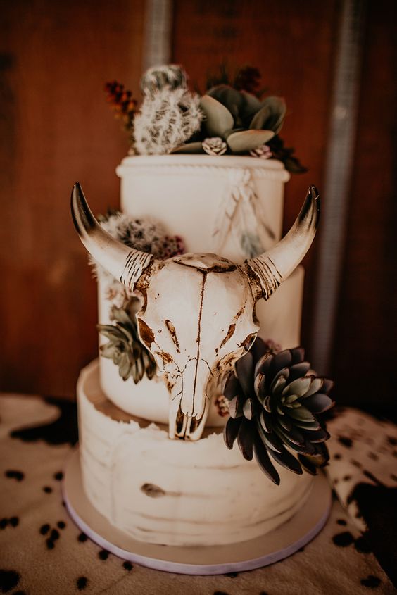 a white wedding cake with succulents and cacti on top, with a skull is a lovely idea for a boho or western wedding