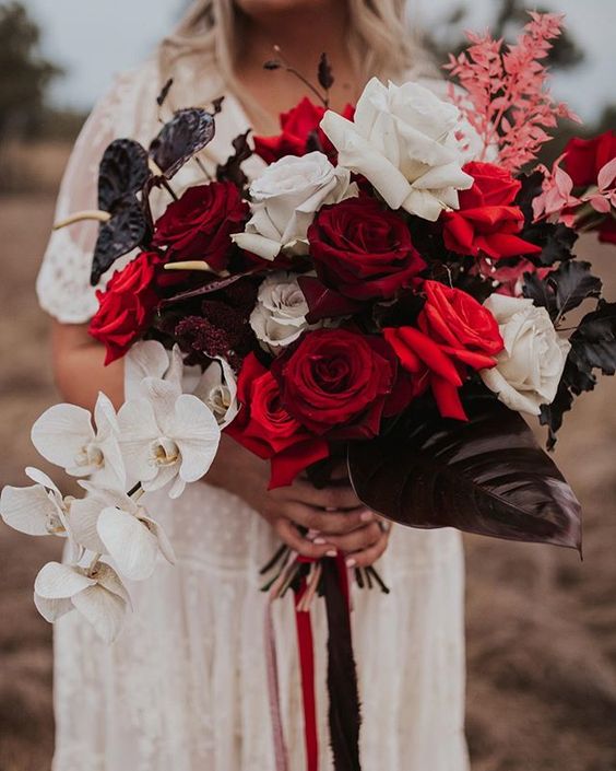 an extra bold and dramatic wedding bouquet of white, red and burgundy roses, dark anthurium and leaves, white orchids and pink foliage