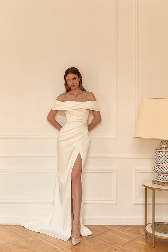 a beautiful and chic off the shoulder wedding dress with a draped neckline, bodice and skirt, a thigh high slit and a train is very sophisticated