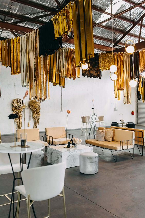 a warehouse wedding lounge with stylish furniture, some blooms and black and gold tinsel fringe over the space