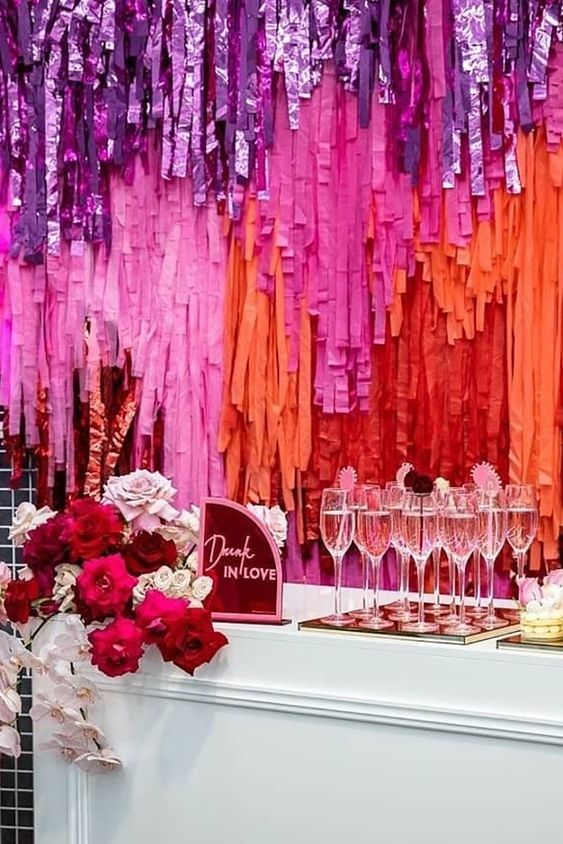 a wedding bar with a super colorful tinsel streamer backdrop, bold blooms and a pink sign is a gorgeous idea for a wedding