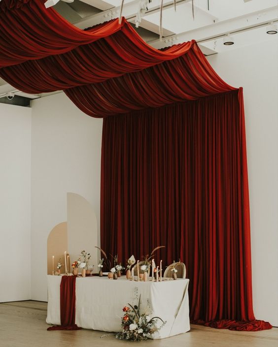 a sophisticated wedding sweetheart table with a burgundy drape over it, a burgundy table runner and lots of candles