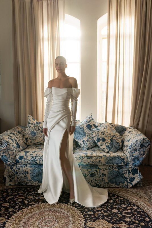 an off the shoulder wedding dress with puff sleeves, a draped bodice and a skirt, a thigh high slit and a train is dramatic