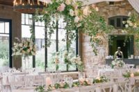 52 an airy and chic wedding reception space with neutral drapes and large chandeliers, white furniture, greenery and white and pink blooms