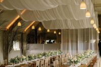 53 an airy wedding reception space with semi-sheer drapes over the space, white table runners, white blooms and greenery